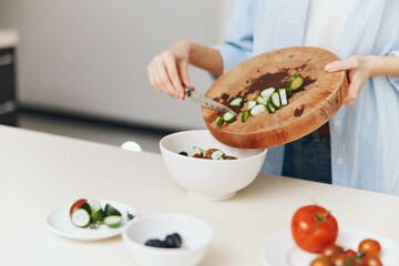 Woman preparing fresh vegetable salad on wooden cutting board with bowl of assorted veggies
