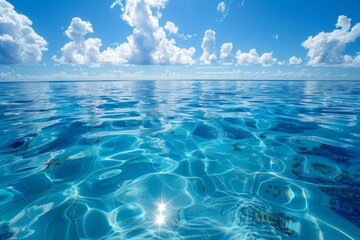 b'Blue ocean water surface with bright sun reflection and white clouds in the background'