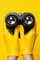b'A person wearing yellow gloves holding a pair of black binoculars' - obrazy, fototapety, plakaty