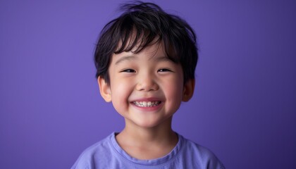 Happy young boy with a tousled hairstyle grinning on a purple colored backdrop