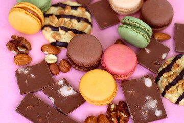Pastel macarons, almond chocolate, peanut butter cookies and various nuts on bright pink background. Selective focus.