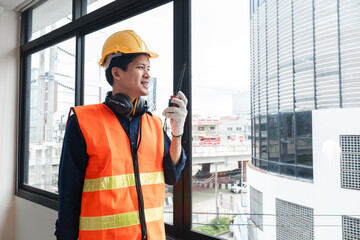 A young engineer stands with a walkie-talkie talking to a team of coordinating engineers at a...