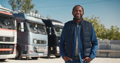 Zooming in on African American mature man in jacket standing at parking lot for lorries and...
