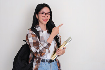 Female college student holding books smiling and pointing beside her