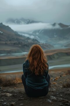b'girl sitting on the edge of a cliff looking at a mountain range'