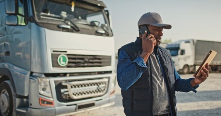 Portrait of african american worker talking by phone in background parked truck vehicles. Truck...