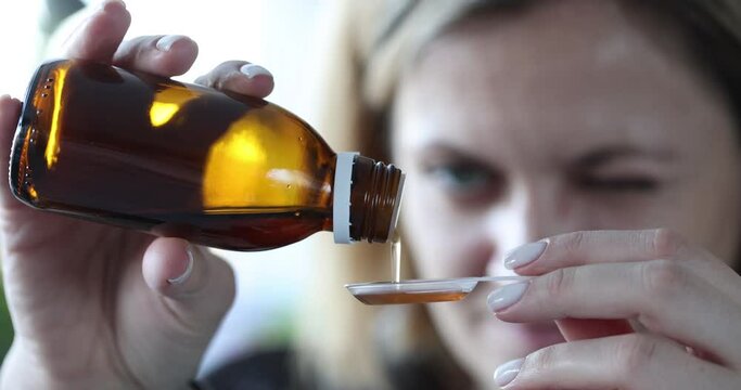 Woman pouring cough syrup into plastic spoon closeup 4k movie slow motion. Cold treatment at home concept