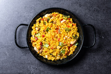 Yellow rice with chicken and vegetables on black slate background