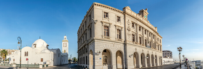 Old building facade with arabic plate says "The Algerian chamber of commerce" and the old great mosque of Algiers. Low angle panoramic view in empty road with nameplate "Saadi et Mokhtar Benhafid".