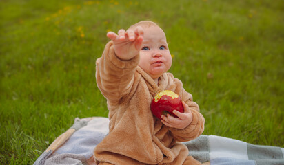 Cute baby girl sitting on plaid and eating apple on the green lawn