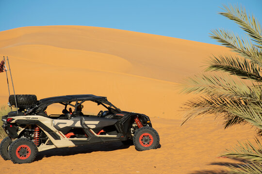 Taghit, Bechar; Algeria - December 27, 2022: Can-Am Maverick XRS buggy car parked in the Sahara desert sand dune. Unrecognizable man wearing a helmet and ski goggles looking at camera inside.