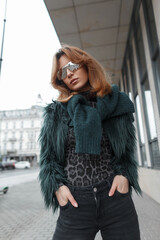 Stylish beautiful fashion vogue model girl with sunglasses in fashionable clothes with a shaggy fur coat with a sweater posing in the city