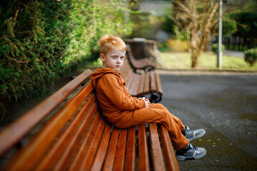 The boy rests on a walk in the garden on a brown bench. Horizontal portrait of a red-haired...