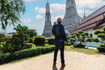 Young Asian traveling backpacker taking photos with camera in Wat Arun in Bangkok, Thailand