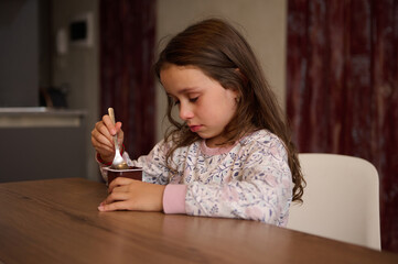 Adorable little child girl eating delicious chocolate vegan yogurt for breakfast. Healthy eating...