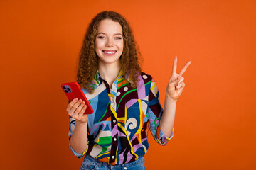 Photo of cheerful cute girl user wear stylish print clothes v-sign symbol isolated on vibrant orange color background