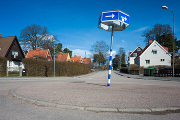 Roundabout on an empty street among Scandinavian style houses, Road sign with white arrows on a blue background, Quiet residential area in sunny day in Sweden