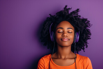 Young African American woman wearing headphones on a purple background listening to her favorite...