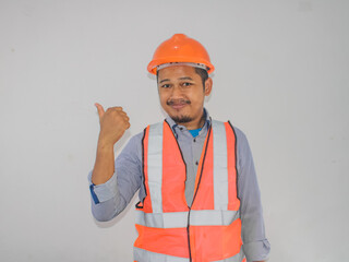 Asian constructor worker man with safety vest  pointing and showing with thumb up to the side with happy face smiling