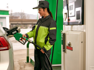 Asian gas station female employee using a gas pump to refuel a car