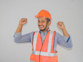 Asian man worker wearing safety helmet lookis happy celebrating his victory by clenching his fists against grey background