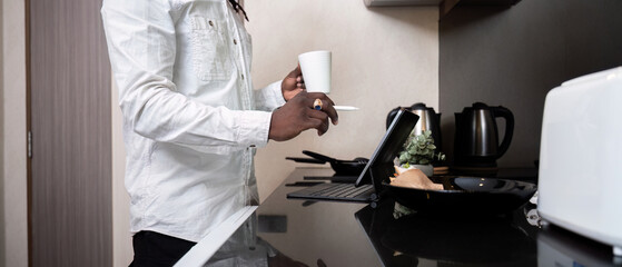 African American man using digital tablet at the kitchen reading social media internet, typing text or shopping online. Freelancer remotely working online at home