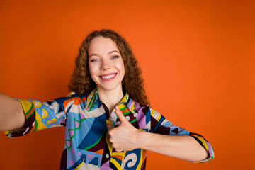 Photo of charming adorable cheerful girl wear trendy print clothes live stream thumb up isolated on vibrant orange color background