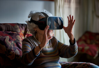 Old lady uses VR headset at her home. Virtual reality, videogames, recreational activities, style, generations, futuristic, technologies. Solitude, connection, internet, cyberpunk.