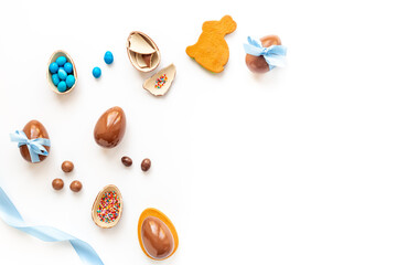 Easter background. Chocolate Easter eggs in blue ribbon with bunny cookies - 796504004