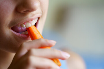 Unrecognizable girl eating fresh carrot slice at home