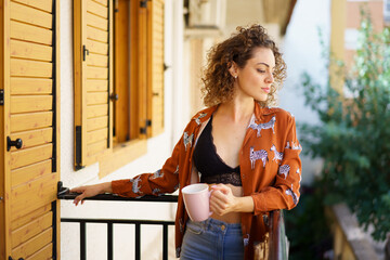 Young woman standing on balcony with cup of coffee - 796511267