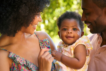 Close Up Of Loving Parents Cuddling Baby Daughter Outdoors In Garden Or Countryside Together