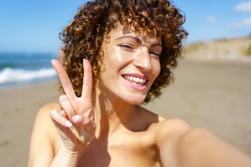 Happy woman showing V sign on beach - 796515678