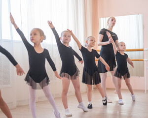 Fototapeta na wymiar Children's ballet school. Caucasian woman teaching ballet to little girls. 