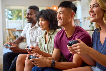Group Of Excited Multi-Racial Friends Sitting On Sofa Playing Computer Games Together
