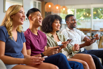 Group Of Excited Multi-Racial Friends Sitting On Sofa Playing Computer Games Together