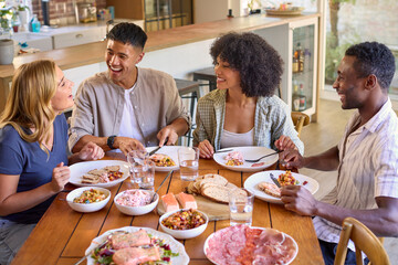 Group Of Multi-Racial Friends Sitting Around Table Enjoying Meal At Home Together