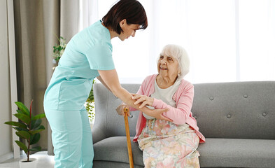 Nurse Hands Cane To Elderly Woman And Helps Her Move Around The Room In A Nursing Home