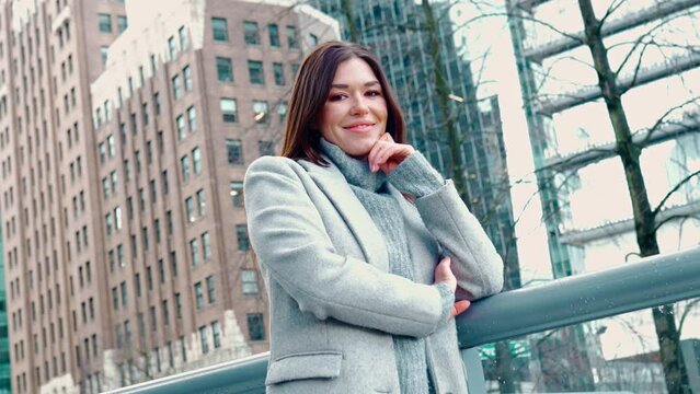 Young smiling professional business woman, happy confident 30 years old lady standing outdoors on big city street business district wearing grey coat, looking at camera, crossing arms, portrait.
