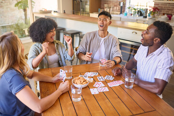 Group Of Multi-Racial Friends Sitting Around Table Playing Game Of Cards At Home Together