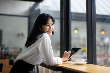 Engaged businesswoman using a digital tablet in a cozy coffee shop setting with a fresh cup of coffee on the table.