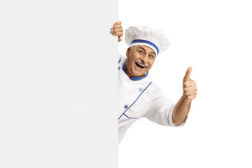 Mature male chef in a uniform gesturing thumbs up behind a blank panel