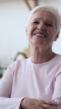 Portrait of a happy senior Caucasian woman, looking and smiling at camera, at home. Mature lady individuality and femininity. Vertical video.