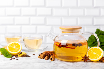 Fragrant hot tea with cinnamon stick and anise on a textured wooden background. A teapot brewing hot tea with honey, lemon, mint and apples. Spicy tea with spices. Immunity tea. Health concept.