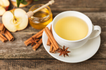 Fragrant hot tea with cinnamon stick and anise on a textured wooden background. A cup of hot tea with honey, lemon, mint and apples. Spicy tea with spices. Immunity tea. Health concept.Copy space.