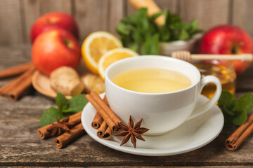 Fragrant hot tea with cinnamon stick and anise on a textured wooden background. A cup of hot tea with honey, lemon, mint and apples. Spicy tea with spices. Immunity tea. Health concept.Copy space.
