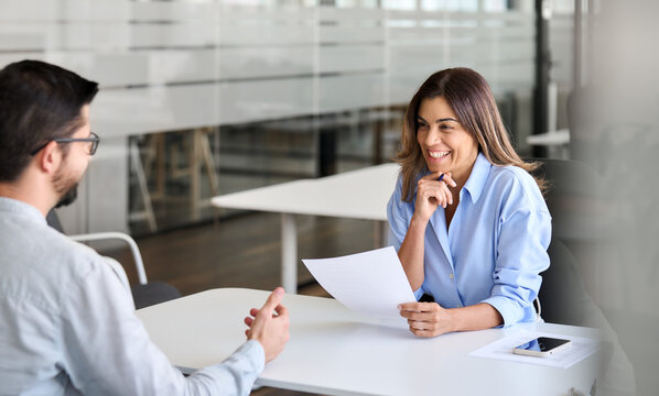 Smiling professional female hr having job interview meeting with male recruit. Happy middle aged business woman financial advisor, bank manager consulting client working in office. Candid photo