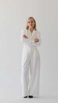 Portrait of a serious and concentrated Caucasian woman in stylish business suit standing with crossed arms on white background. Vertical video.