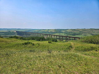 Non-urban landscape overlooking a wide valley of green grass with a long railroad trestle bridge spanning it and a clear blue sky.
