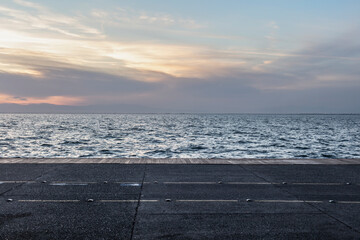A concrete promenade borders the sparkling sea under a gradient sunset sky, merging urban with...